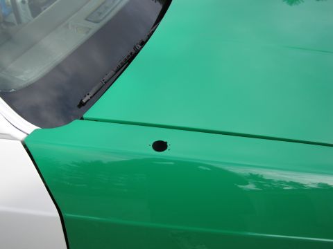 1991 Ford LTD Crown Victoria - Close-up of a green-painted rear body panel meeting a white pillar, with a small black fuel filler cap and the base of the windshield.
