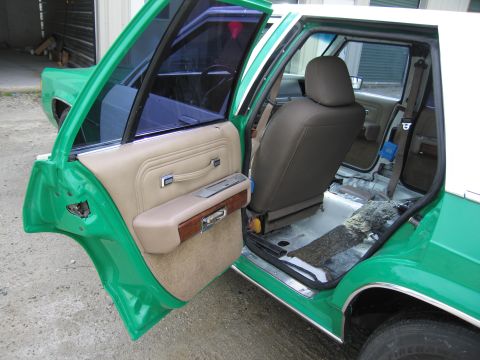1991 Ford LTD Crown Victoria - open rear door of a green-and-white sedan revealing a tan door panel with woodgrain and a dark cloth seat.