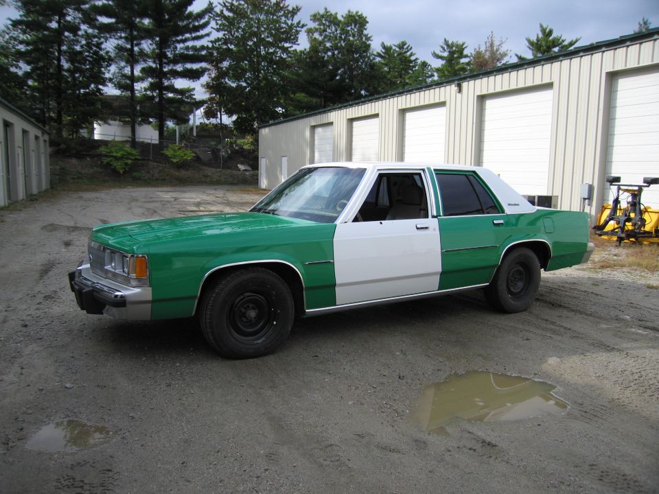 Green and white two-tone Ford sedan front three-quarter view on gravel lot