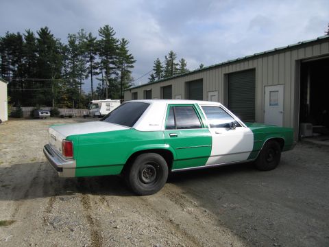 1991 Ford LTD Crown Victoria - two-tone green-and-white sedan seen from the rear-right parked on gravel in front of metal garage doors.