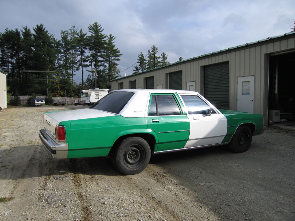 Green and white sedan rear three-quarter view outside metal garage