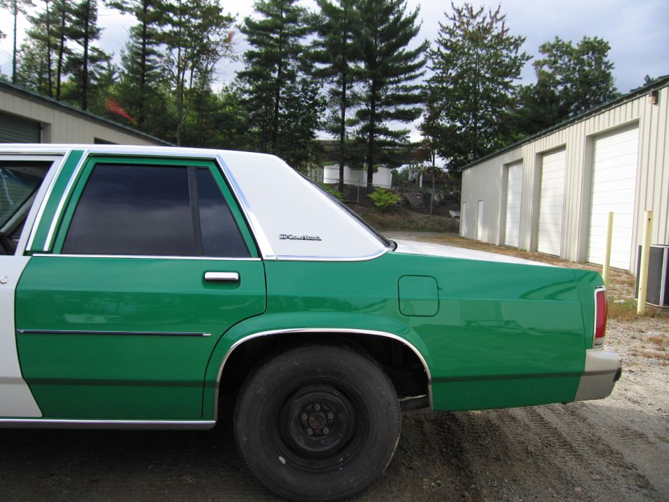 Rear side of green and white sedan with Crown Victoria badge on door