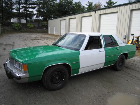 1991 Ford LTD Crown Victoria - two-tone green-and-white four-door sedan parked at an angle on gravel in front of metal storage buildings.