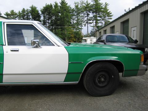 1991 Ford LTD Crown Victoria - front door and fender of a green-and-white sedan with a chrome mirror, a dark vehicle parked behind it.