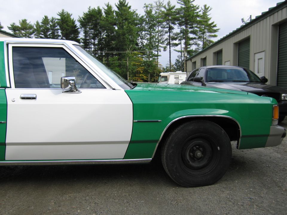 Front side of green and white sedan with chrome mirror; dark car behind