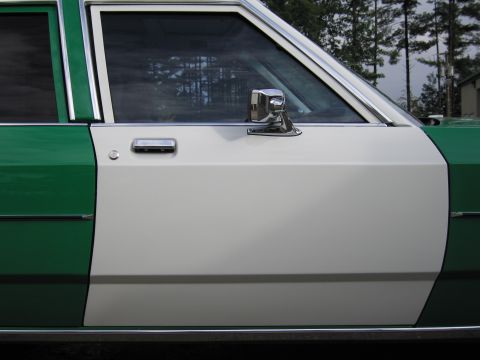 1991 Ford LTD Crown Victoria - Close-up of the white rear door and chrome side mirror of a green-and-white sedan with tinted windows.