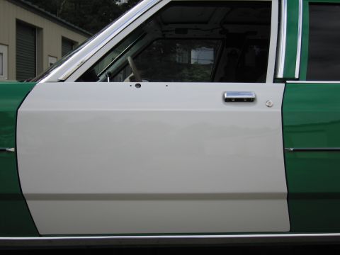 1991 Ford LTD Crown Victoria - Close-up of the white front door and chrome handle of a green-and-white sedan, with storage units in the background.