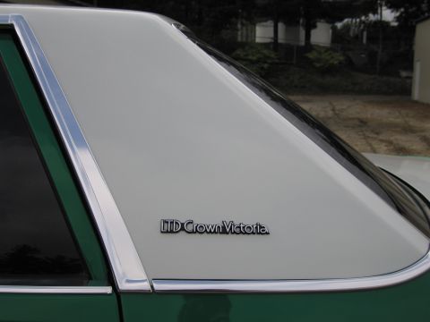 1991 Ford LTD Crown Victoria - Detail of a green sedan's rear quarter window and C-pillar showing a chrome-framed "LTD Crown Victoria" nameplate.