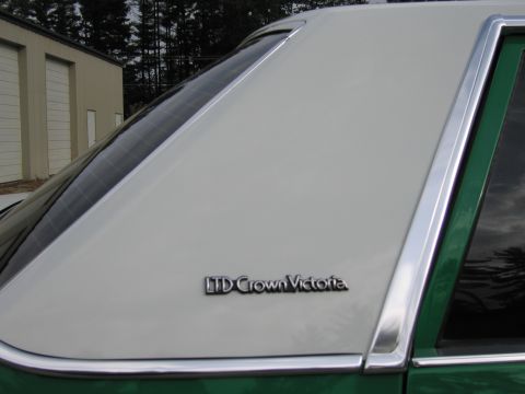 1991 Ford LTD Crown Victoria - green sedan's vinyl-look rear roof pillar and quarter glass bearing an "LTD Crown Victoria" badge, shot near a metal building.