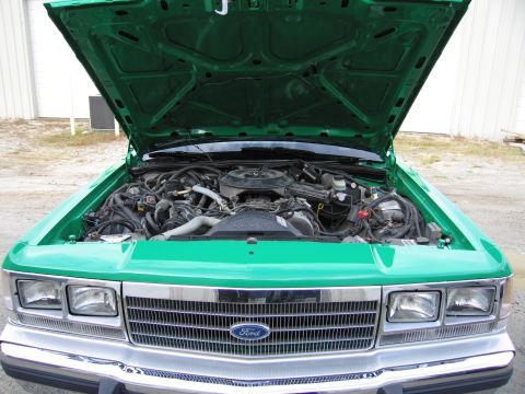 1991 Ford LTD Crown Victoria - Head-on shot of a green Ford sedan with hood up, showing the engine, dual headlights and a chrome grille bearing the Ford oval.