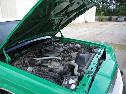 1991 Ford LTD Crown Victoria - Open engine compartment of a green car showing the round air cleaner, hoses and exposed inner fender with the hood raised.
