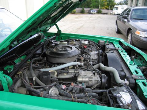 1991 Ford LTD Crown Victoria - Engine bay of a green car under a raised hood, with a gray sedan and a motorhome parked in the lot behind.