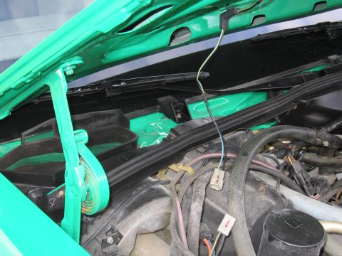 1991 Ford LTD Crown Victoria - Under-hood detail of a green car showing the cowl panel, wiper arm linkage, a green hood prop and engine wiring.