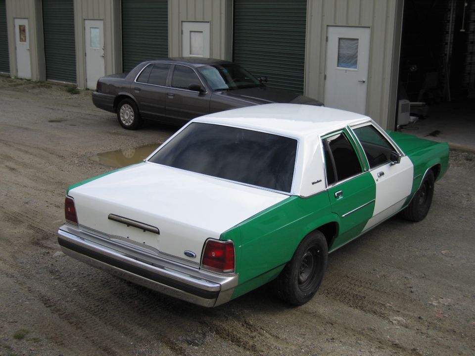 Rear three-quarter of white and green Ford sedan at storage units