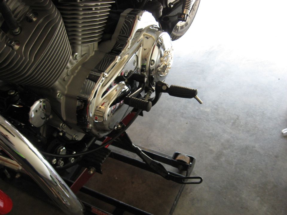 Chrome motorcycle primary cover with foot peg and controls on a lift stand