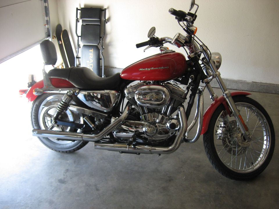 Red Harley-Davidson Sportster with chrome pipes and laced front wheel in a garage