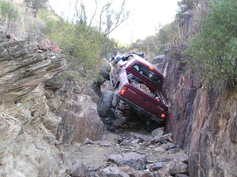 1986 Toyota Hilux - This Toyota pickup is navigating a challenging rocky terrain, with one side significantly higher than the other.