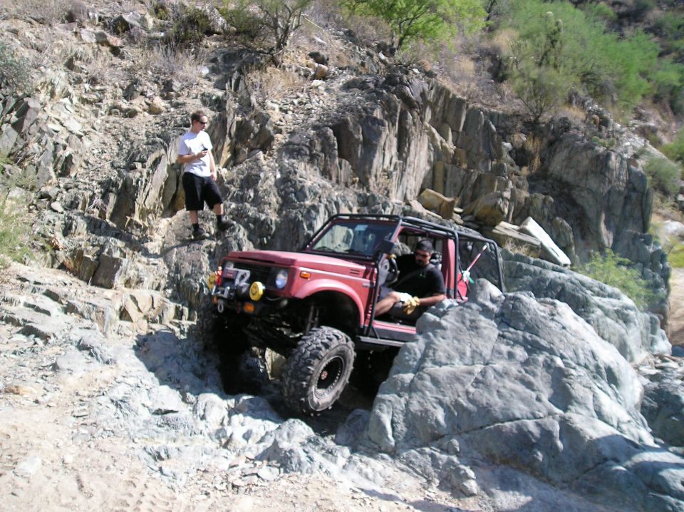 Red off-road vehicle with a roll cage on a rocky trail, driver visible
