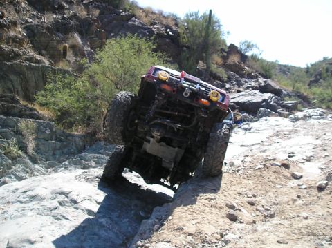 1986 Toyota Hilux - This off-road truck navigates a challenging rocky path, showing its undercarriage and front end.