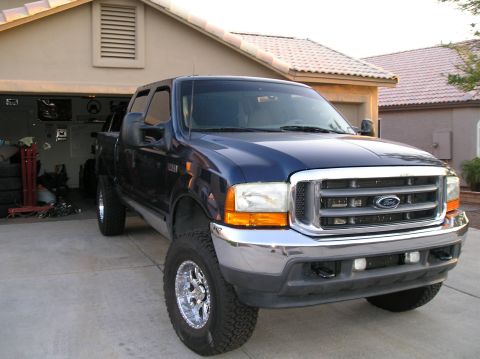 2001 Ford F-350 - This blue 2001 Ford F-350 pickup truck is shown from a 3q-front angle, parked in a driveway with a garage in the background.