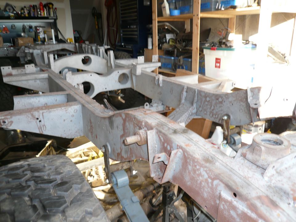 Bare rusty vehicle chassis frame stripped down in a cluttered garage