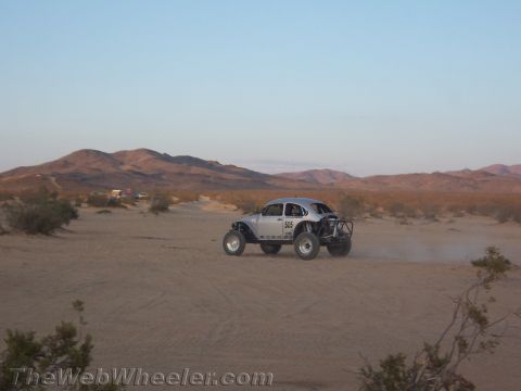 1990 Ford Bronco - silver Baja Bug speeds across the open desert at dusk, trailing a faint cloud of dust.