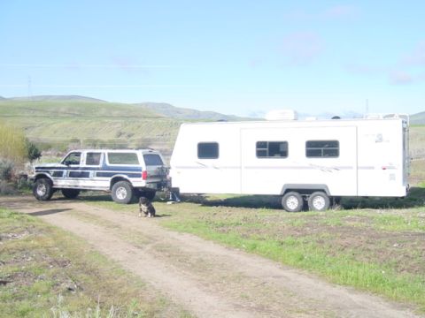 1994 Ford C-350 (Centurion Conversions) - A blue and white Ford Bronco SUV is parked next to a large white travel trailer on a dirt road.
