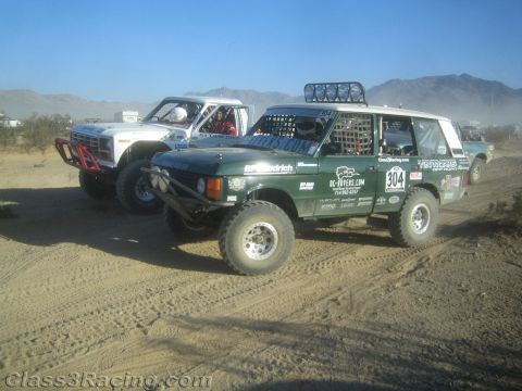 1990 Ford Bronco - green Range Rover racer numbered 304 and a white off-road truck sit side by side on a dusty desert course.