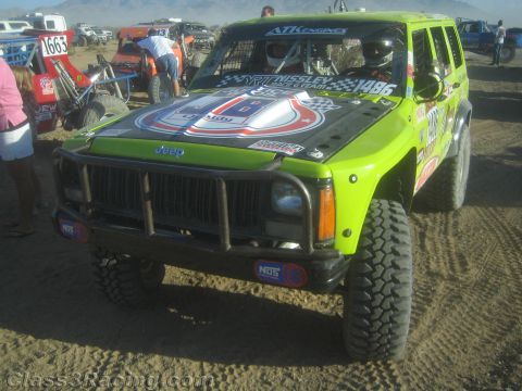1990 Ford Bronco - bright green Jeep Cherokee prepped for off-road racing, numbered 1496 with a brush bar, sits in a dusty desert staging area.