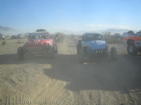 1990 Ford Bronco - red off-road buggy and a blue Baja Bug numbered 512 line up amid heavy dust in the open desert.