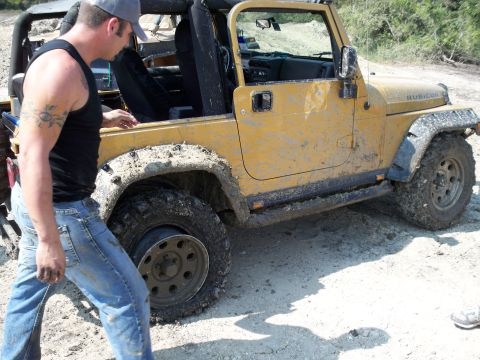 1996 Ford Bronco - Mud-covered yellow Jeep Wrangler with a man standing nearby on a dirt road.