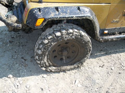 1996 Ford Bronco - A muddy gold Jeep Wrangler is shown from the side, with its front wheel and fender prominently displayed.