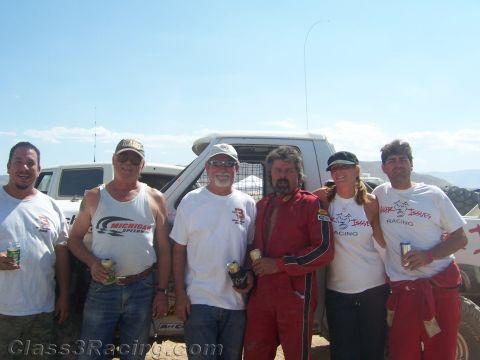 1990 Ford Bronco - Six people in casual and racing clothes pose together holding drinks in front of a white truck at a desert venue.