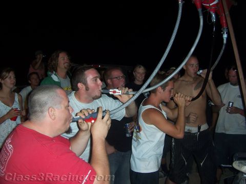1990 Ford Bronco - Young men drink from hoses connected to an overhead funnel rig at a crowded nighttime desert party.