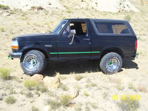 1993 Ford Bronco - This black Ford Bronco is parked on a rocky, desert-like terrain. It has off-road tires and a green stripe along its side.