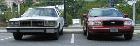 1985 Ford Crown Victoria LTD - Two sedans are parked side-by-side in a parking lot, with one vehicle appearing older than the other.