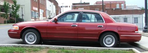 1985 Ford Crown Victoria LTD - This red sedan is parked on a street with buildings in the background.