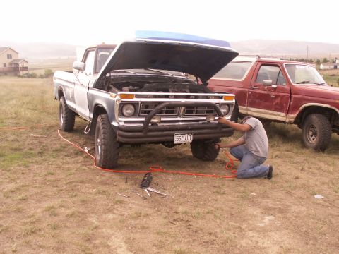 1977 Ford F-250 - A man works on the engine of a 1977 Ford F-250 pickup truck, with another truck parked beside it.