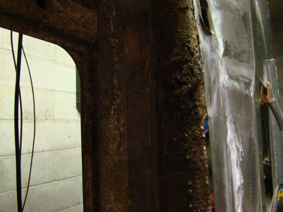 Rusted metal frame with visible wiring and a section of shiny metal, possibly undergoing repair