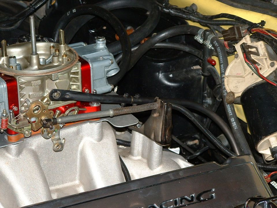 Close-up of a vehicle's engine bay showing a carburetor, intake manifold, and various hoses and wires