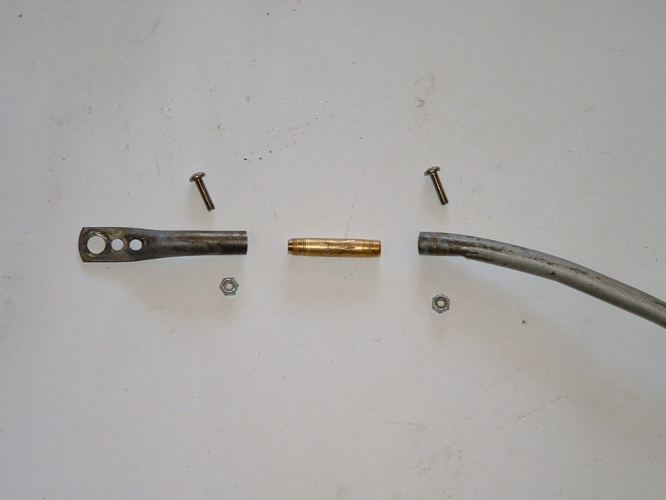 Disassembled metal linkage with brass bushing, screws, and nuts on a white surface