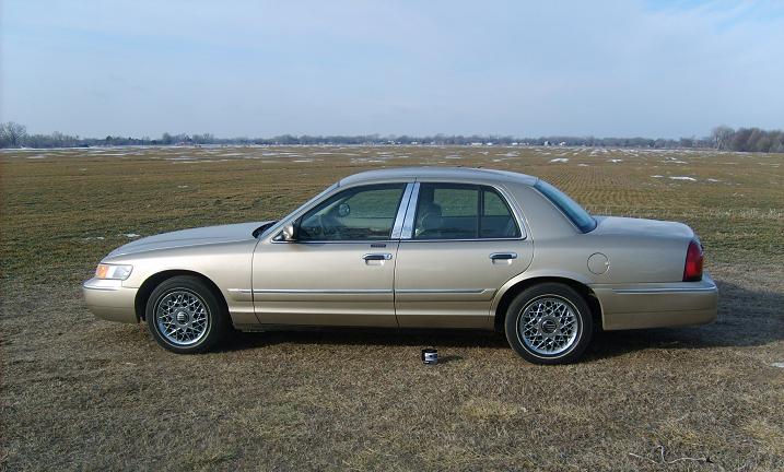 Driver-side profile of gold Mercury Grand Marquis sedan on mesh wheels in a winter field