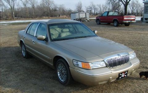2000 Mercury Grand Marquis - A gold 2000 Mercury Grand Marquis is parked outside with a red pickup truck in the background.