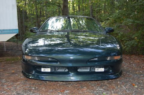 1996 Ford Probe - This dark green coupe is parked in a wooded area, showing its front end with pop-up headlights.