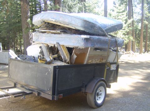 1986 Ford Bronco - A trailer is filled with discarded mattresses and other debris, parked outdoors in a wooded area.