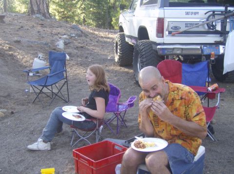 1986 Ford Bronco - A lifted Ford Bronco is parked at a campsite where two people are eating meals.