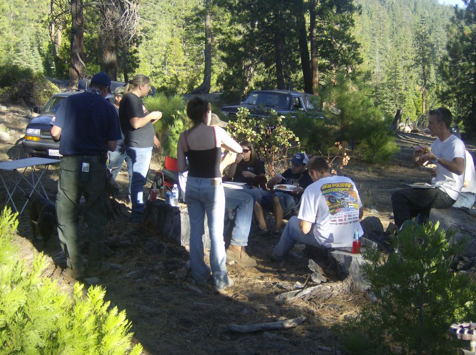 Dark blue Ford Bronco parked in a wooded area with people gathered around