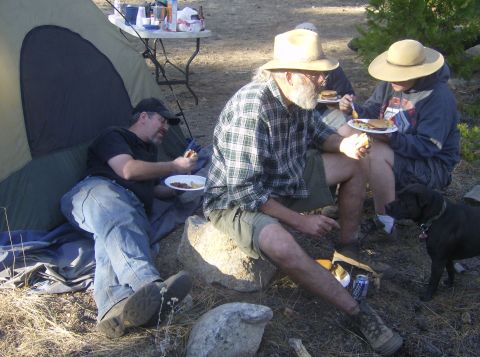 1986 Ford Bronco - A group enjoys a meal outdoors at a campsite, with a tent set up and a dog observing.