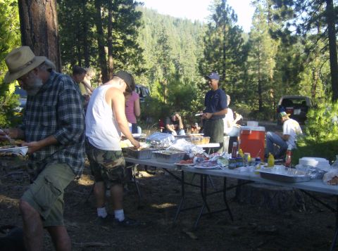 1986 Ford Bronco - A group enjoys a picnic in a wooded area, with a dark SUV visible behind the tables.
