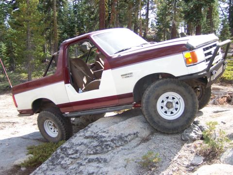 1991 Ford Bronco - This modified Ford Bronco navigates a challenging rocky trail in a wooded area.